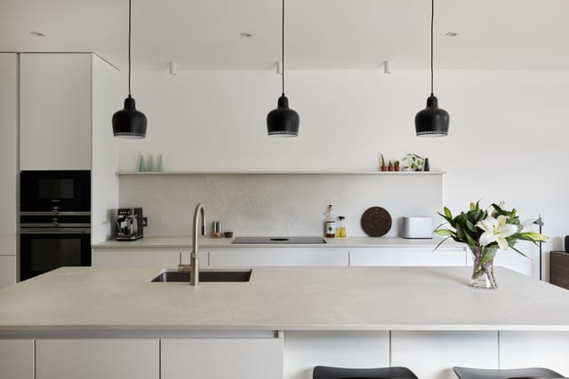 A calm, light piqu kitchen with a brushed-brass mixer and black pendant lights.
